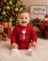 A baby sitting on a white faux fur rug in front of a decorated Christmas tree, wearing a red long-sleeve romper with a Santa graphic and the name 'Jason' in gold script.