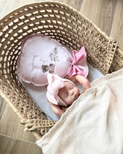 Newborn baby in a Moses basket with pink headband and outfit