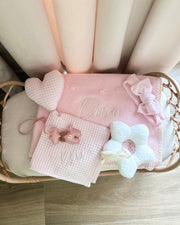 Baby crib with pink and white bedding, including a blanket and pillow, on a wooden floor.