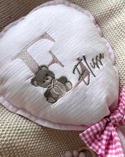 Heart-shaped pillow with embroidered teddy bear and text on a textured surface
