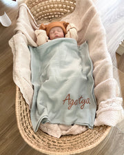 Newborn baby wrapped in a blanket with 'Agata' embroidered, lying in a woven basket.