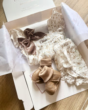 Baby outfit with floral pattern and brown bow in a box on a wooden surface