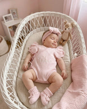 Baby in a pink outfit sleeping in a wicker chair with a teddy bear.