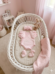 Baby outfit set with pink romper, socks, and headband in a white crib with teddy bear and pink bedding.