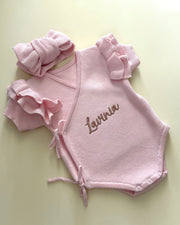 Pink baby outfit with ruffles and 'Lavinia' embroidery on a light green background