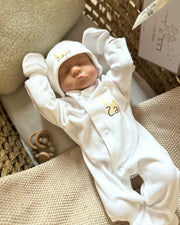 Newborn baby in a white outfit with name embroidery and wooden heart teether - Eli&Eli