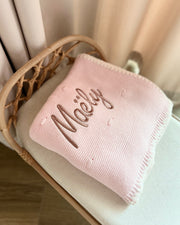 Pink baby blanket with embroidered name on a white surface