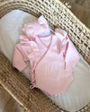 Pink baby outfit with ruffles on a textured surface