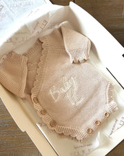 Knitted baby romper with bib in a box on a wooden surface