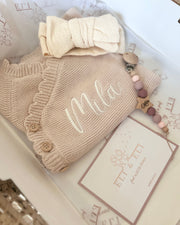 Knitted baby outfit with 'Mila' on a textured surface