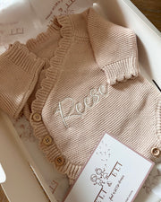 Knitted baby sweater with 'Rose' embroidery on a white surface
