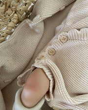 Close-up of a beige knitted garment with buttons on a textured surface