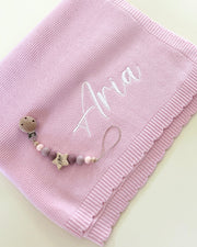 Pink baby blanket with 'Aria' embroidered on it, accompanied by a pacifier clip.