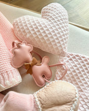 Baby hat, booties, and bib with a pink theme on a textured surface