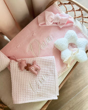 Pink and white baby blanket with decorative elements on a wooden surface