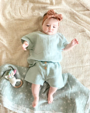 Baby wearing sage green shirt and short rainbow muslin cotton fabric